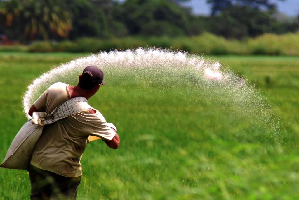 Agriculteur épandant des intrants dans un champ, illustration de l’impact du MACF sur les engrais et les coûts agricoles